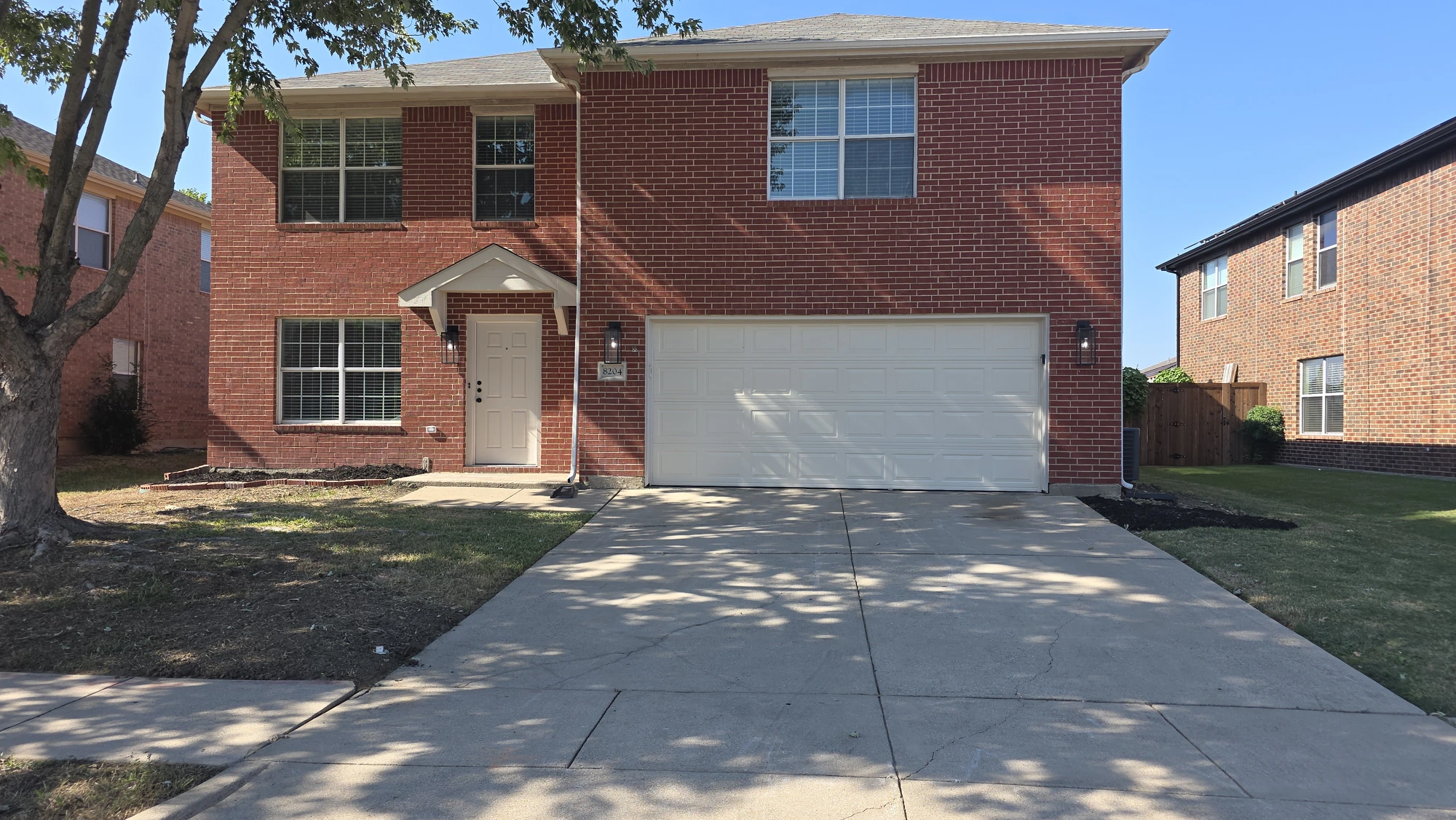 Before investor rehab: front exterior of a two-story red-brick home with a white two-car garage door, white front door, and house number 8204 in the Mansfield TX area