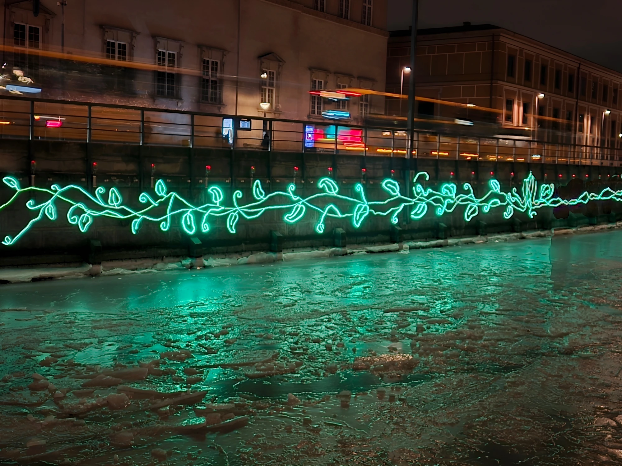 A glowing green Copenhagen Light Festival installation on the quay, reflected in the icy harbour at night
