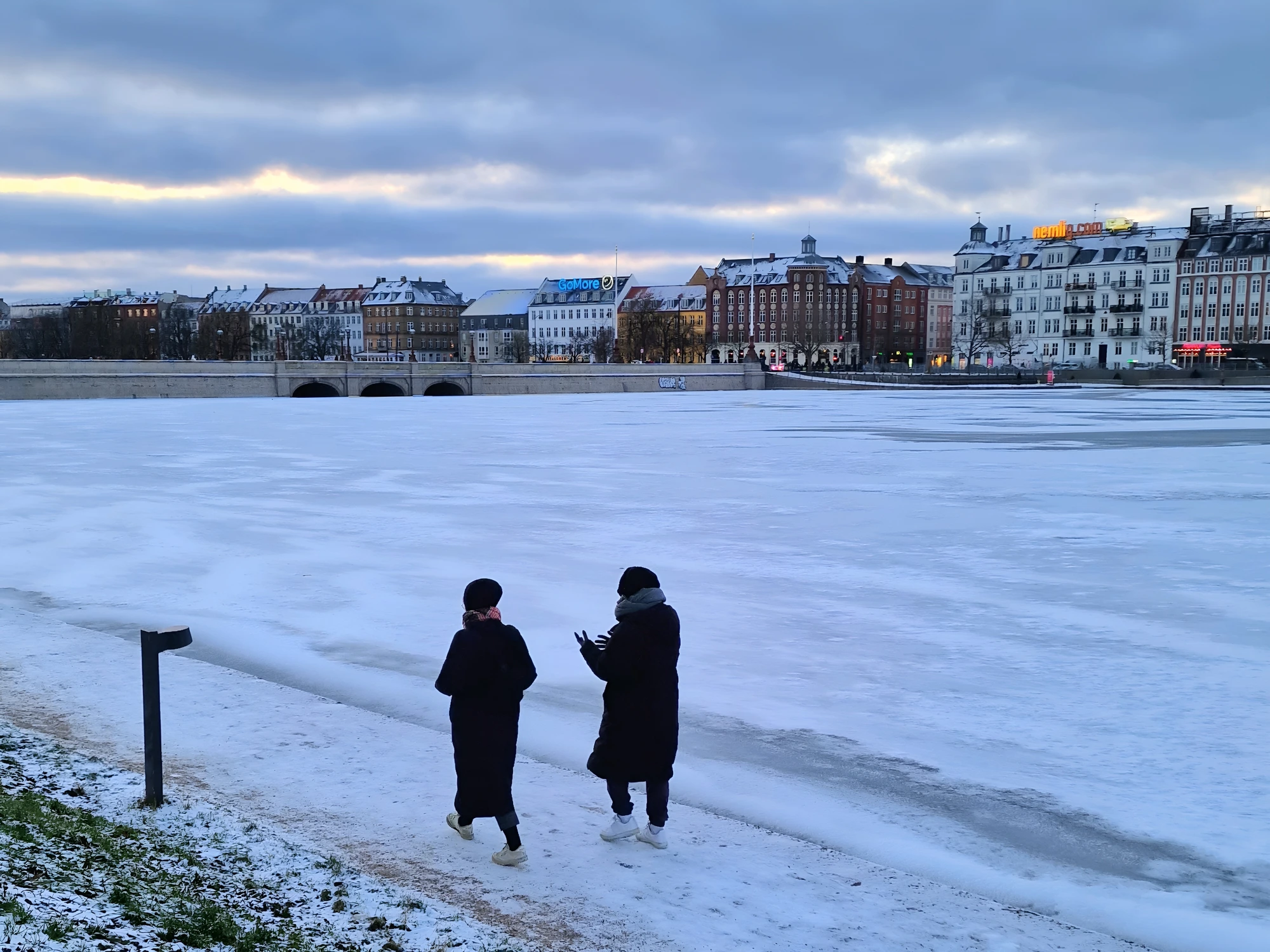 The frozen Copenhagen Lakes in January — walkers on the ice with the snow-covered Nørrebro skyline beyond