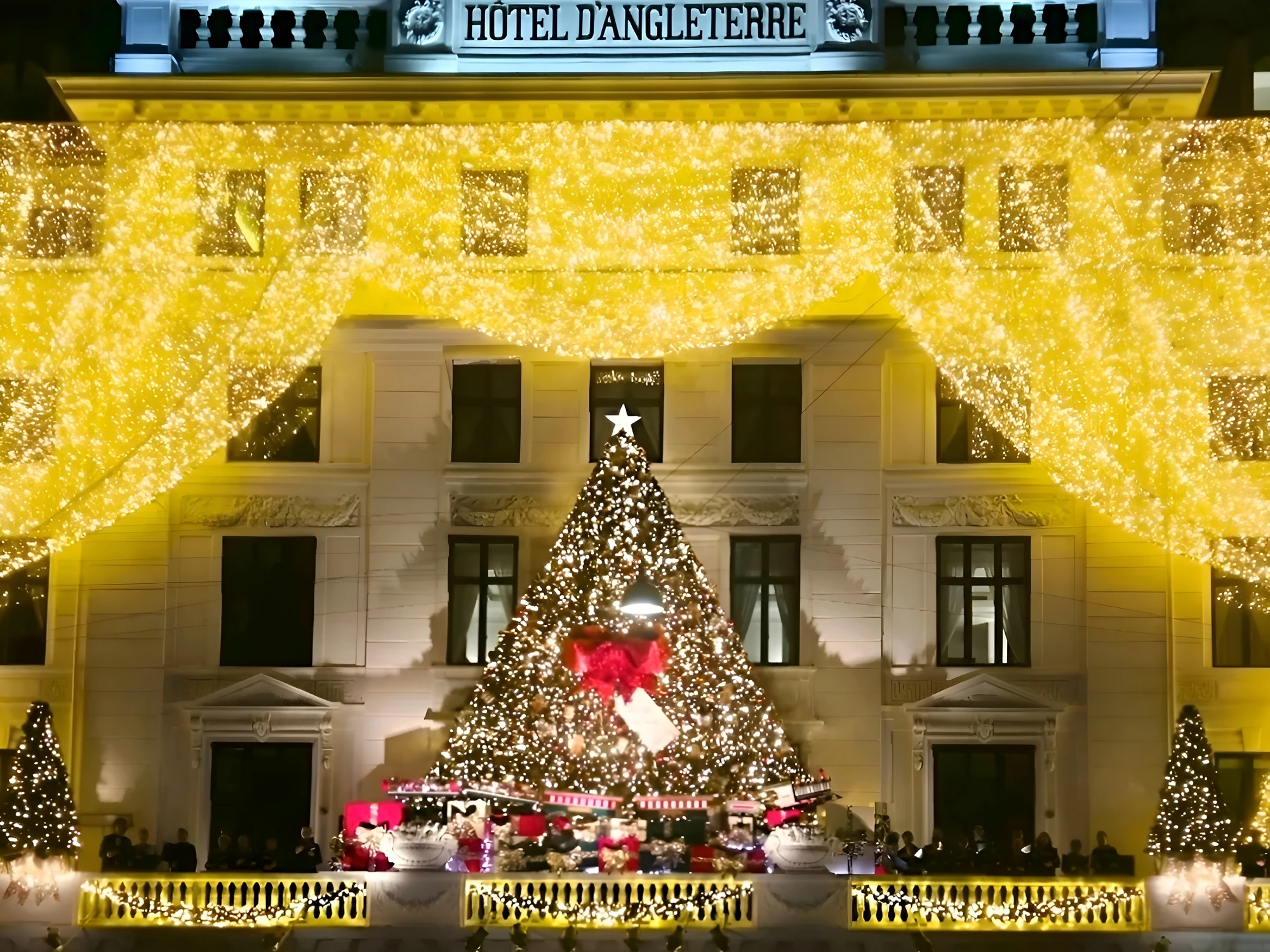 Hotel d'Angleterre's façade wrapped in golden Christmas lights with a huge Christmas tree outside