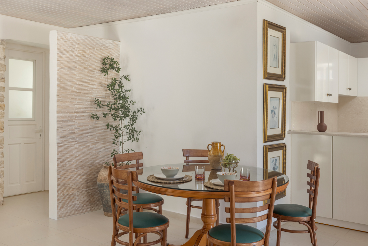Dining table — glass top, framed botanicals, olive branches, kitchen just beyond