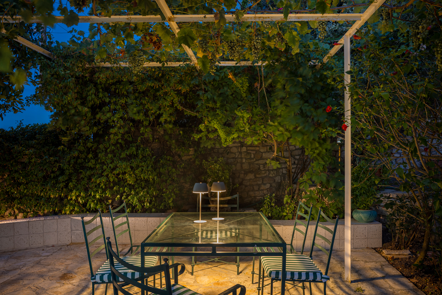 Pergola dining at dusk, two warm lamps glowing