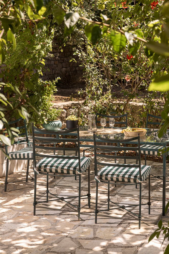 Pergola dining glimpsed through the vine leaves in the midday sun — striped cushions, glass table below