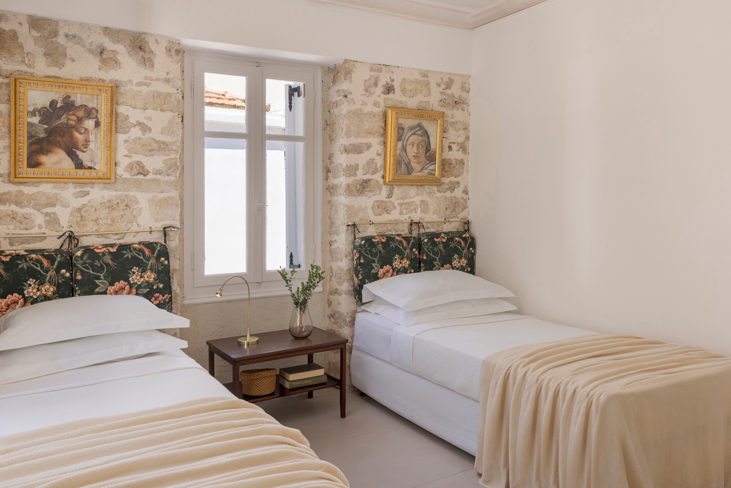 Second bedroom — twin beds with green floral headboards, exposed stone walls, framed Renaissance portraits
