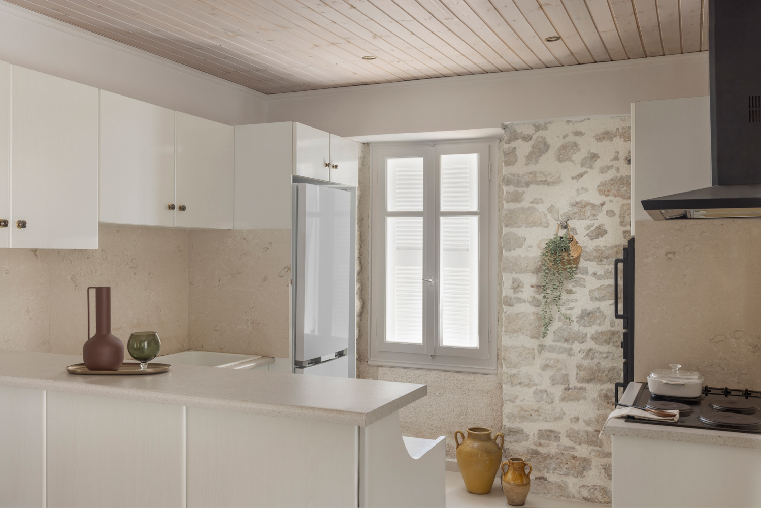 Kitchen — white cabinetry against an exposed-stone accent wall, shuttered window, amphoras on the counter