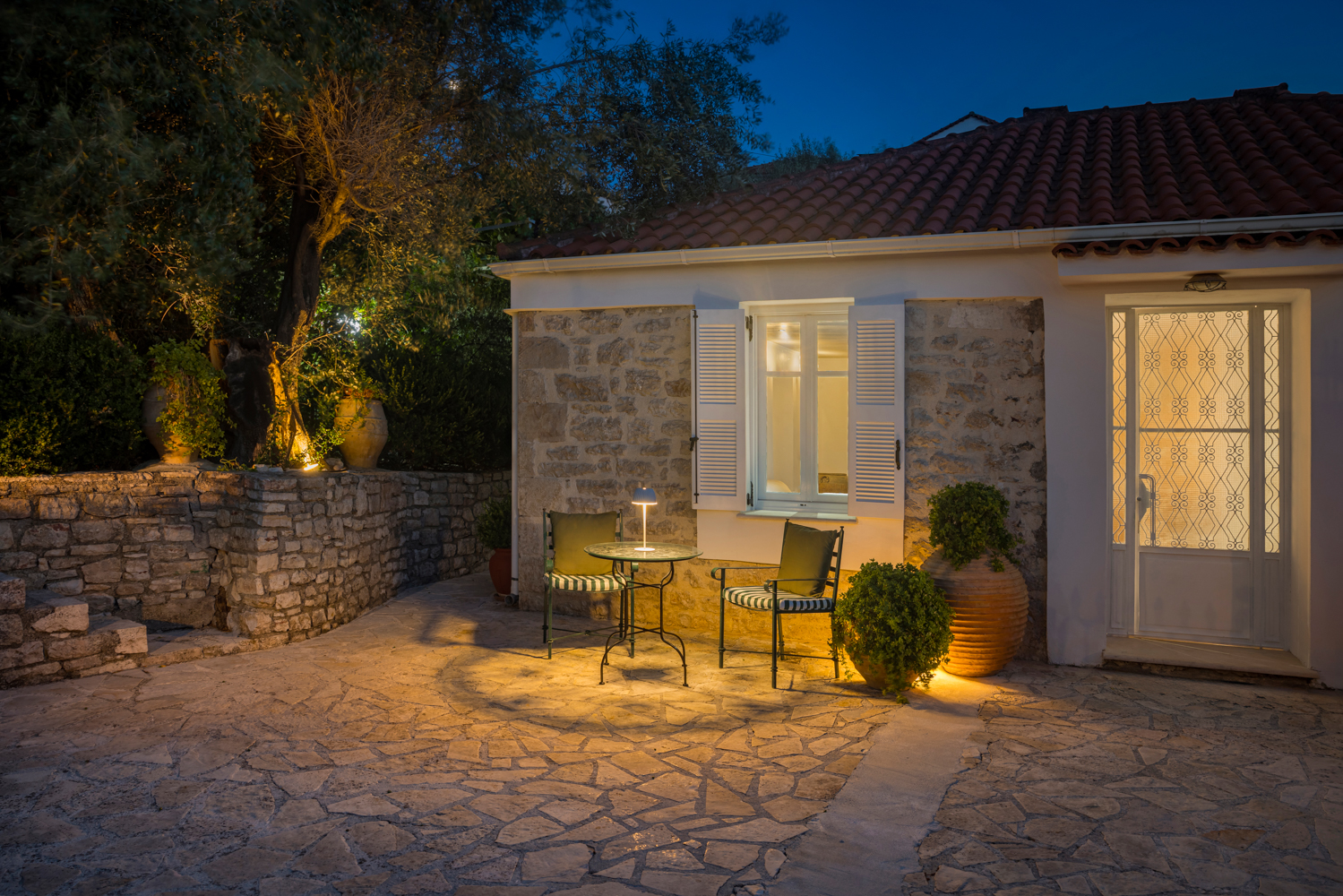 Evening bistro table by the stone wall — Ithaca Garden Villa, Kioni