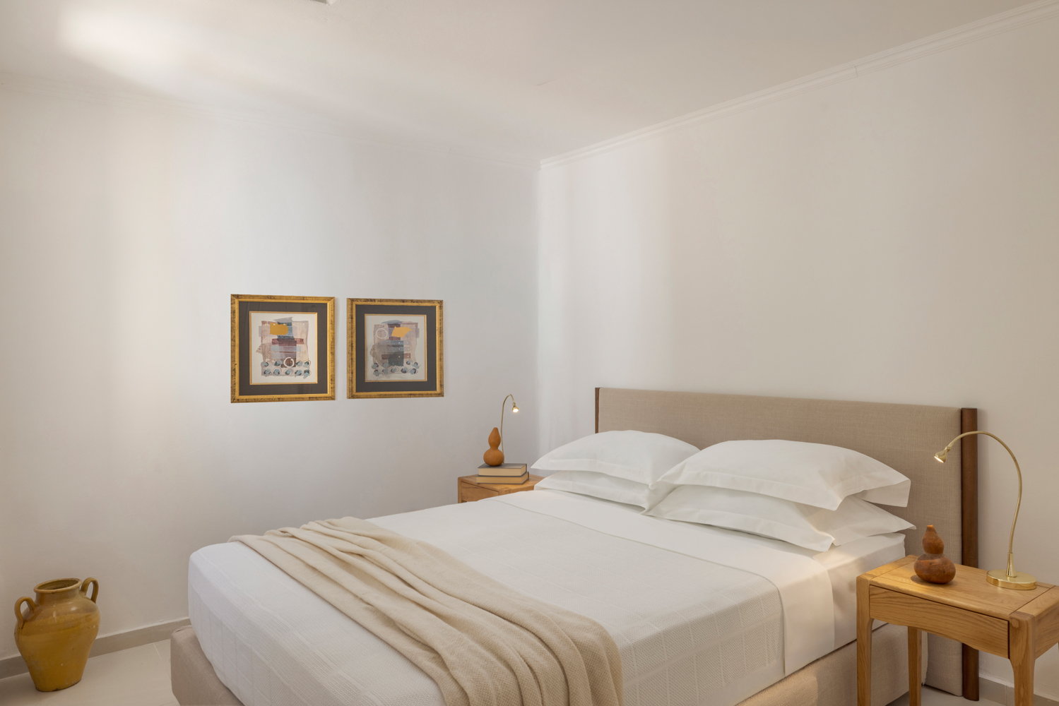 The guest bedroom — cream headboard, framed abstract art, brass reading lamps