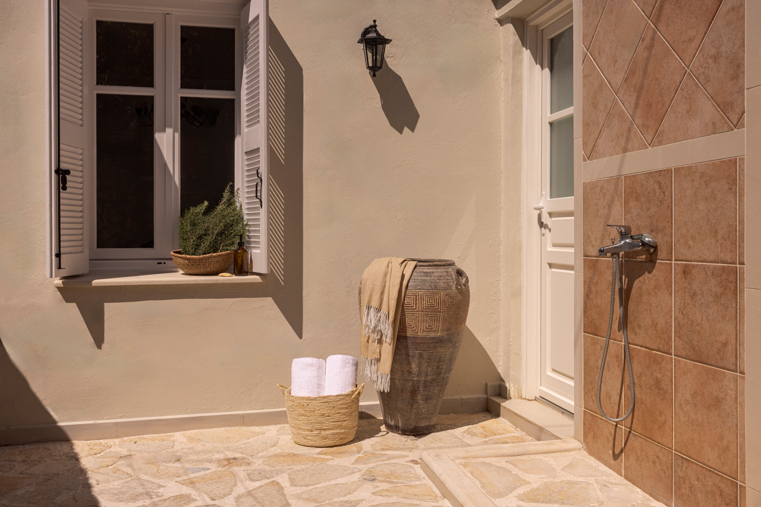 Sunlit outdoor shower area with amphora and rolled towels
