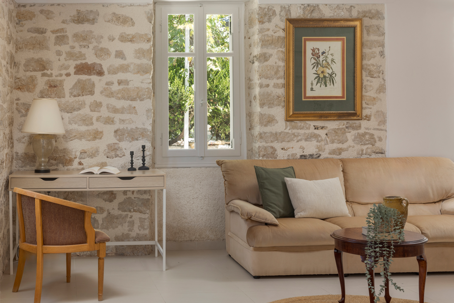 Sitting corner — light-wood writing desk with lamp, botanical print on exposed stone, single sofa and woven chair