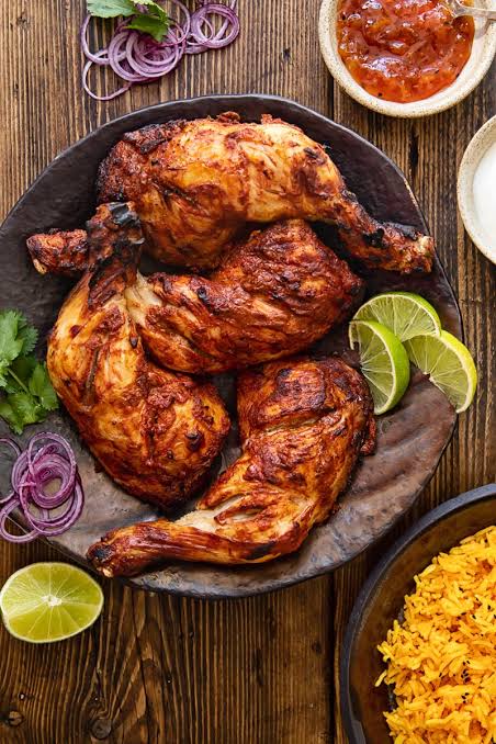Charred tandoori chicken legs with lime wedges and sliced onions
