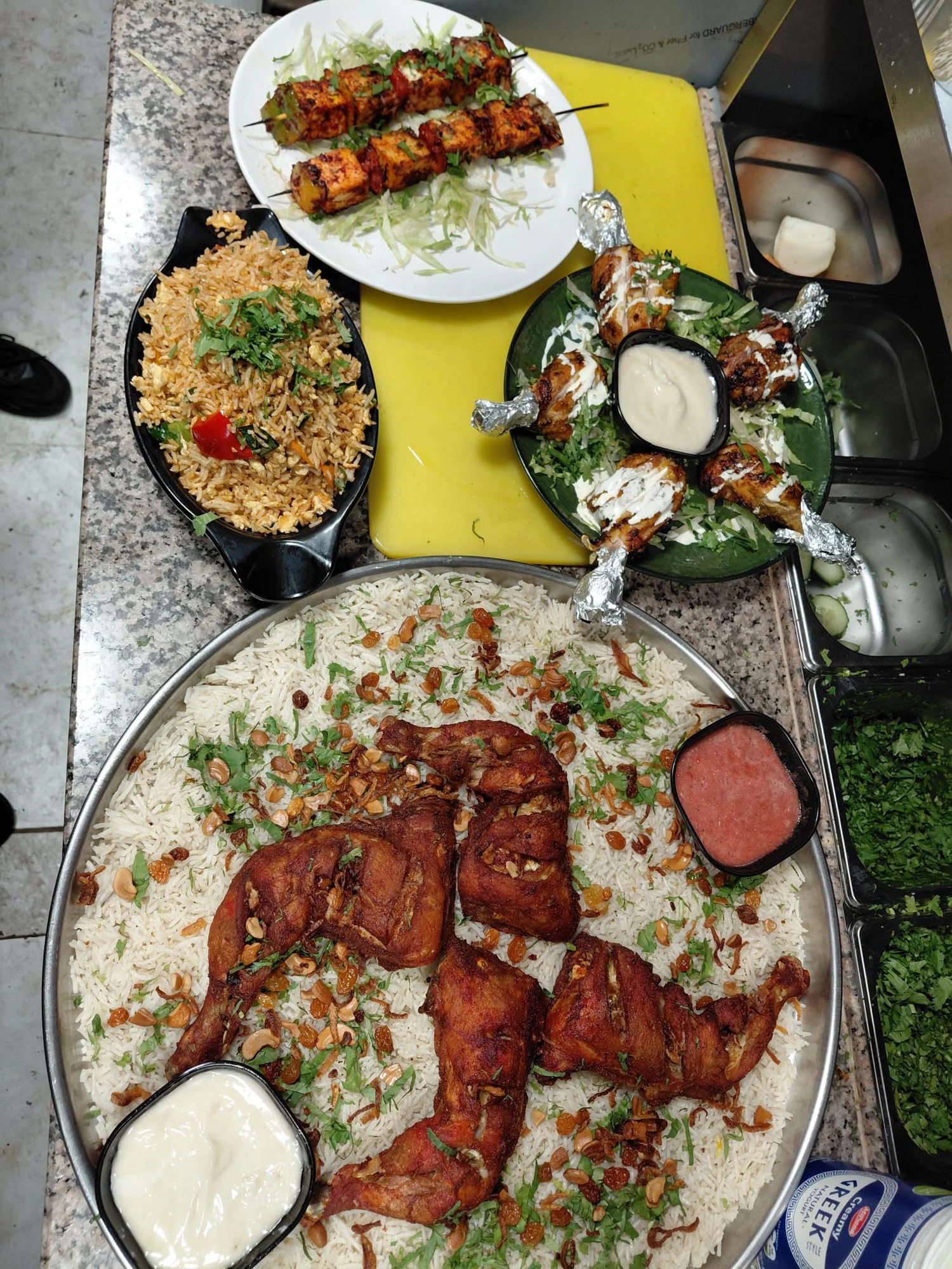 Arabian mandi spread: a large platter of rice topped with roasted chicken, served with skewers, fried rice and sauces