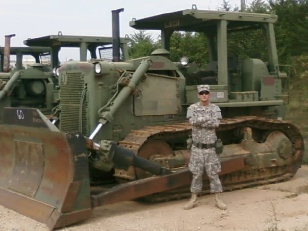 Greg in uniform in front of a military bulldozer