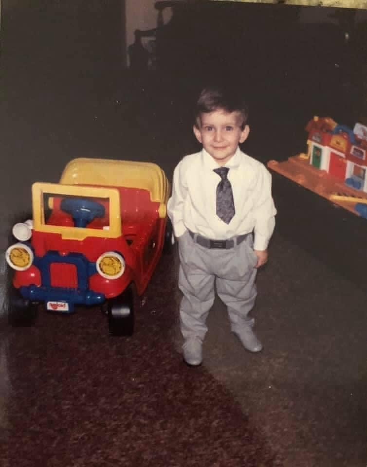 Toddler Greg in dress shirt & tie next to a toy car